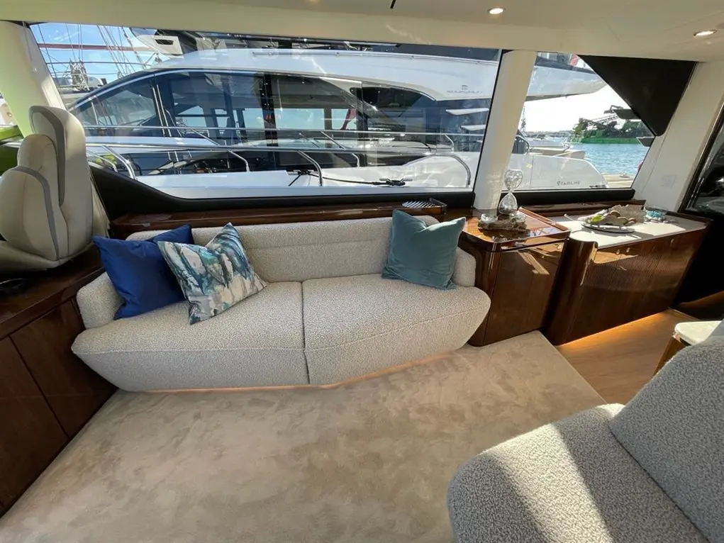 Luxurious yacht interior featuring a grey sofa with decorative cushions, wooden cabinets, and a view of boats outside.